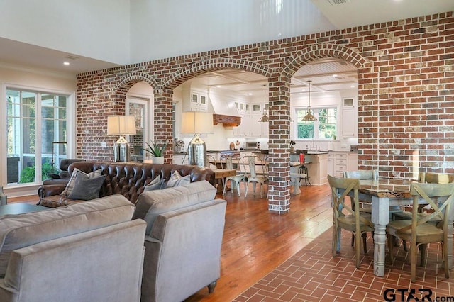 living area with a towering ceiling, brick wall, and wood finished floors