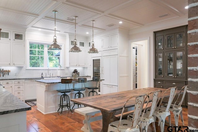 kitchen with glass insert cabinets, white cabinets, a kitchen island, dark stone countertops, and coffered ceiling