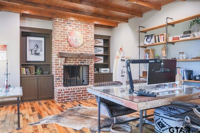 office area with a brick fireplace, wooden ceiling, light wood-style flooring, and beam ceiling