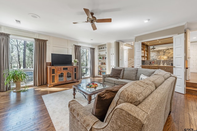 living area featuring ceiling fan, dark wood-type flooring, visible vents, built in features, and ornamental molding