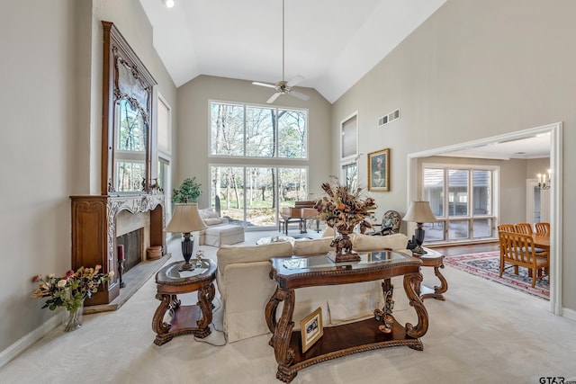 living room with visible vents, a fireplace with raised hearth, carpet flooring, high vaulted ceiling, and ceiling fan with notable chandelier