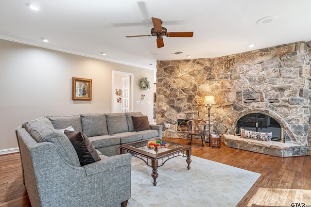 living area with crown molding, visible vents, ceiling fan, a stone fireplace, and hardwood / wood-style flooring