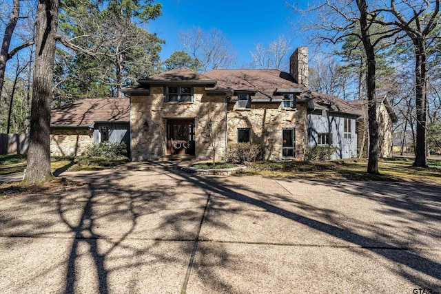 view of front facade featuring stone siding, a chimney, and driveway