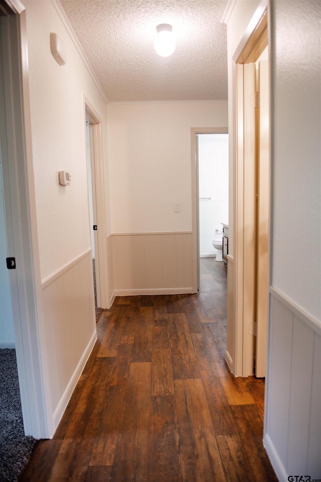 hallway featuring dark wood-type flooring, a textured ceiling, and crown molding