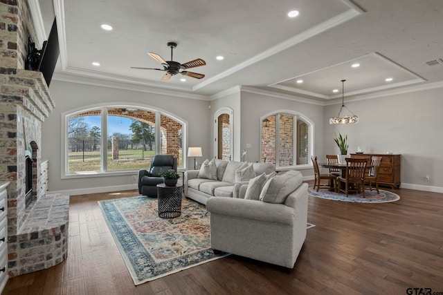 living room with dark wood-type flooring, a fireplace, ceiling fan, and crown molding