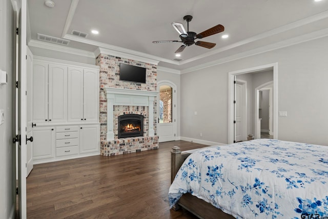 bedroom featuring a brick fireplace, ceiling fan, crown molding, and dark hardwood / wood-style flooring