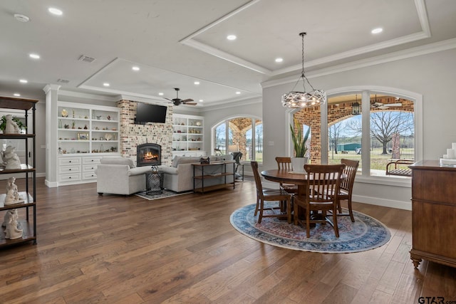 dining area with dark wood-type flooring, a fireplace, crown molding, and ceiling fan