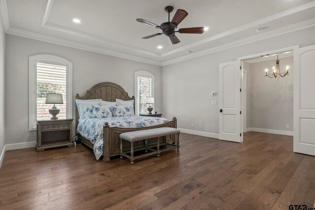 bedroom with dark wood-type flooring, ceiling fan with notable chandelier, crown molding, and a tray ceiling