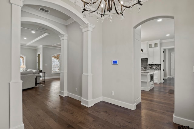 hall featuring dark wood-type flooring, decorative columns, and ornamental molding