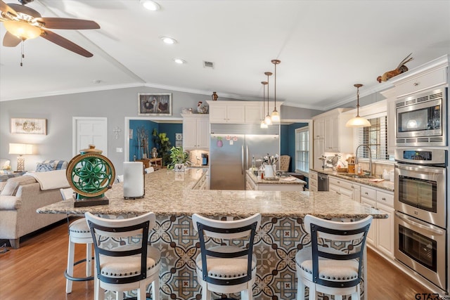 kitchen with built in appliances, a breakfast bar, sink, light stone counters, and hanging light fixtures