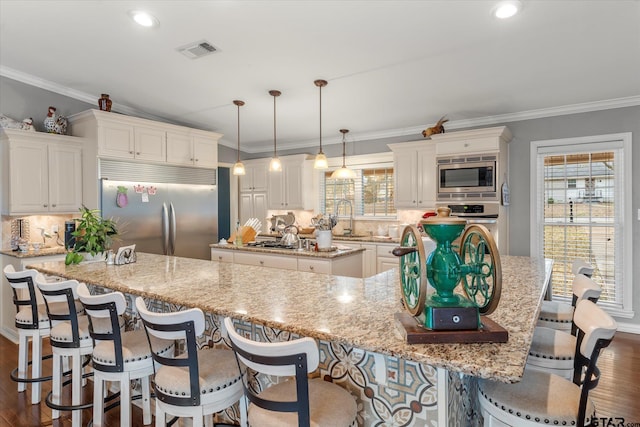 kitchen featuring a large island, hanging light fixtures, built in appliances, light stone counters, and white cabinets