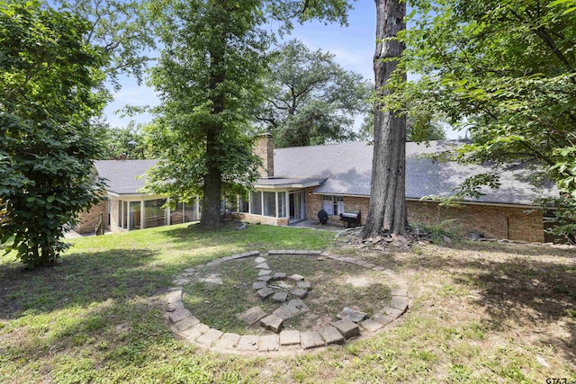 1723 Kensington Dr, Tyler, TX 75703 - rear view of property featuring a sunroom, a chimney, brick siding, a shingled roof, and a lawn
