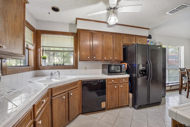 802 Carriage Dr, Tyler, TX 75703 - kitchen with black appliances, tile countertops, brown cabinetry, a textured ceiling, and light tile patterned floors