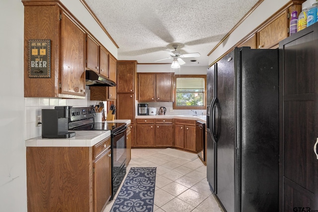 802 Carriage Dr, Tyler, TX 75703 - kitchen with black appliances, ceiling fan, brown cabinets, tile counters, and a textured ceiling
