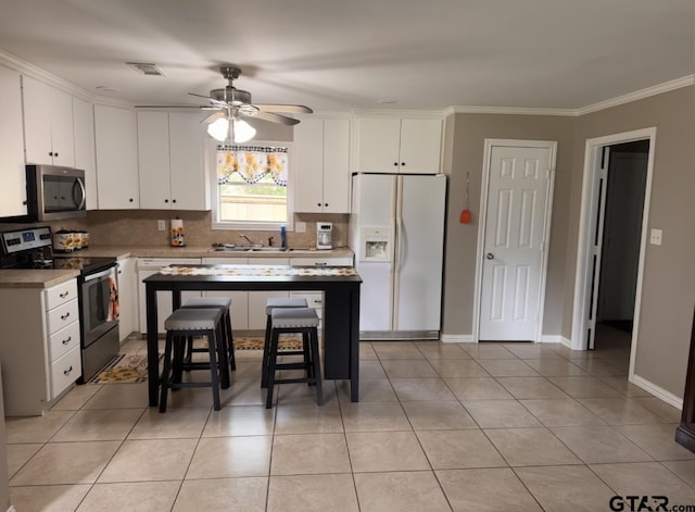 kitchen featuring crown molding, ceiling fan, appliances with stainless steel finishes, a kitchen bar, and backsplash