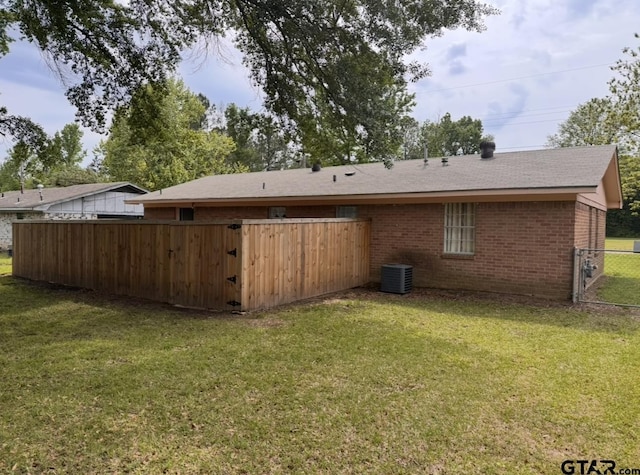 back of house with roof with shingles, a lawn, central AC unit, brick siding, and fence