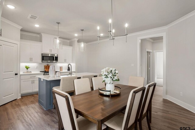 dining space featuring dark wood-type flooring, sink, an inviting chandelier, and ornamental molding