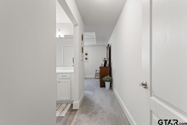 hallway featuring light colored carpet and baseboards