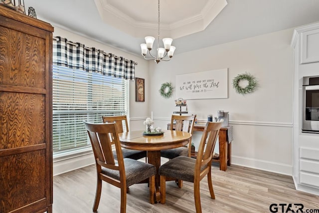 dining space featuring a chandelier, light wood-type flooring, a raised ceiling, and crown molding