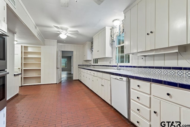 2318 S Chilton Ave, Tyler, TX 75701 - kitchen with white dishwasher, brick floors, ceiling fan, white cabinets, and tile counters
