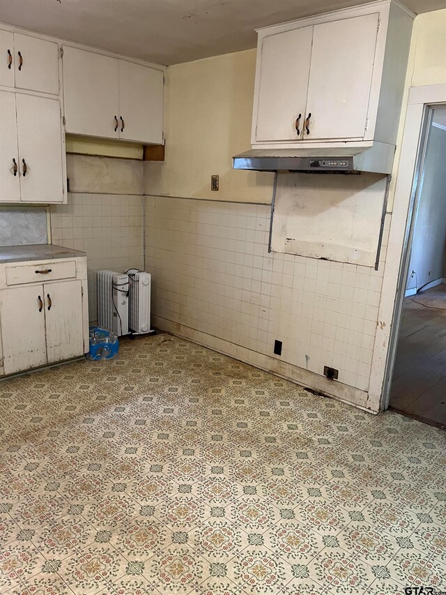 kitchen with white cabinets, tile walls, and radiator