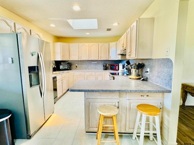 kitchen with backsplash, kitchen peninsula, stainless steel fridge with ice dispenser, a kitchen breakfast bar, and a skylight