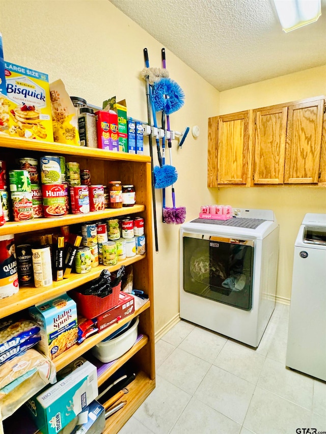 clothes washing area featuring cabinets, a textured ceiling, washer and dryer, and light tile patterned floors