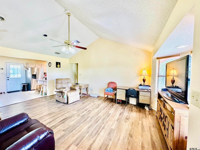 living room with light wood-type flooring, vaulted ceiling, ceiling fan, and a textured ceiling