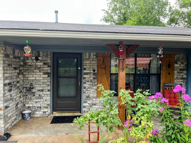 219 Lockhart St, Pittsburg, TX 75686 - doorway to property featuring covered porch, brick siding, and a shingled roof