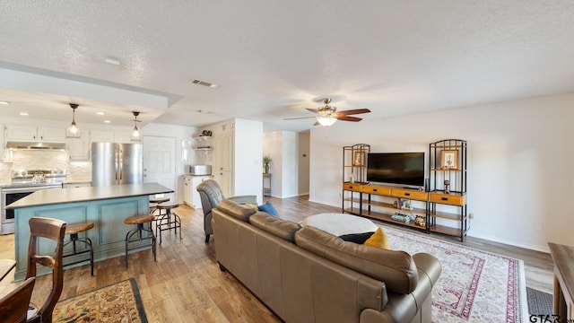 living room featuring ceiling fan, light hardwood / wood-style flooring, and a textured ceiling