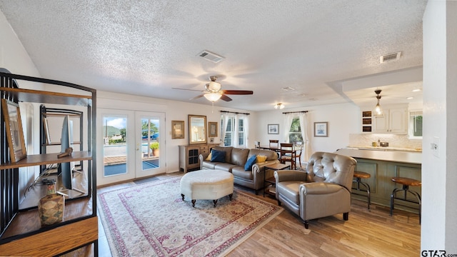 living room featuring a textured ceiling, light hardwood / wood-style flooring, french doors, and ceiling fan