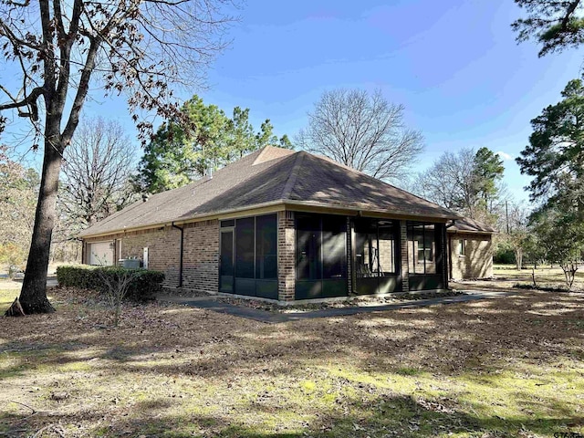 back of house featuring an attached garage, a sunroom, a shingled roof, and brick siding