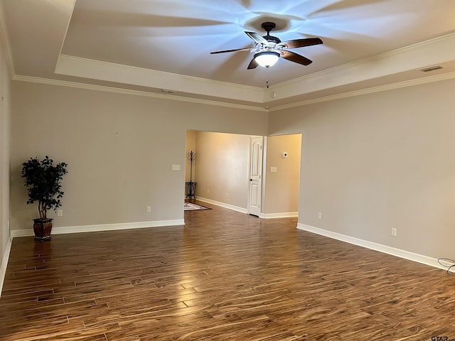 empty room with a ceiling fan, baseboards, ornamental molding, dark wood-style floors, and a raised ceiling