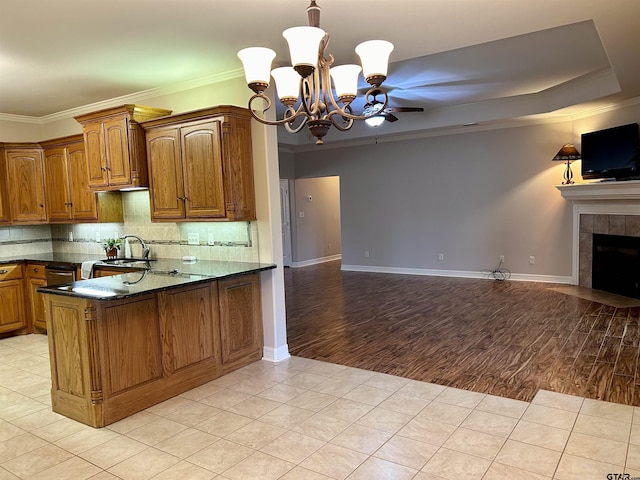 kitchen with light tile patterned floors, brown cabinetry, a tile fireplace, open floor plan, and crown molding