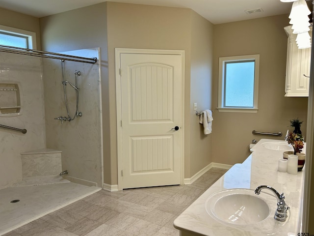 full bathroom with a marble finish shower, double vanity, visible vents, a sink, and baseboards