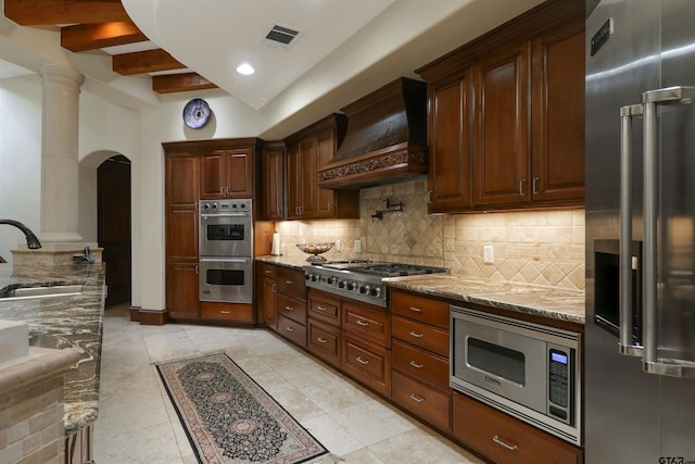 kitchen with sink, light stone counters, appliances with stainless steel finishes, light tile patterned floors, and premium range hood