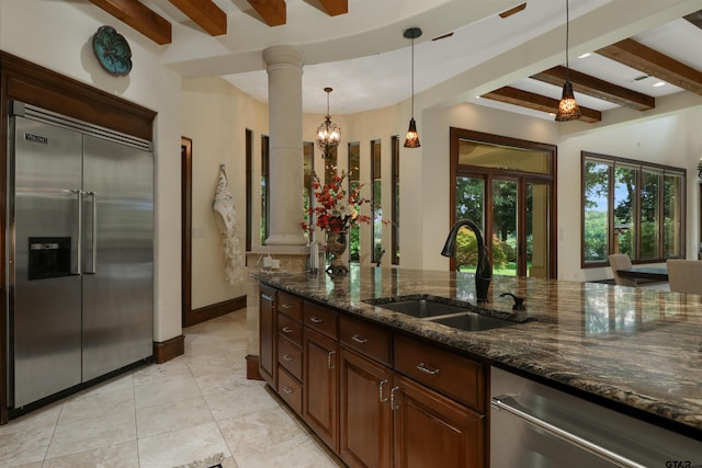 kitchen featuring stainless steel appliances, decorative light fixtures, beam ceiling, sink, and dark stone countertops