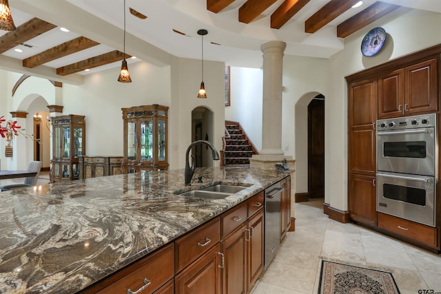 kitchen with sink, beamed ceiling, pendant lighting, appliances with stainless steel finishes, and dark stone countertops