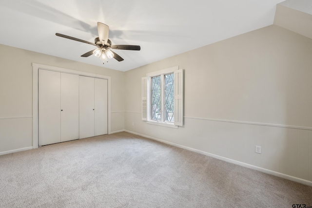 unfurnished bedroom featuring baseboards, lofted ceiling, carpet flooring, a closet, and a ceiling fan