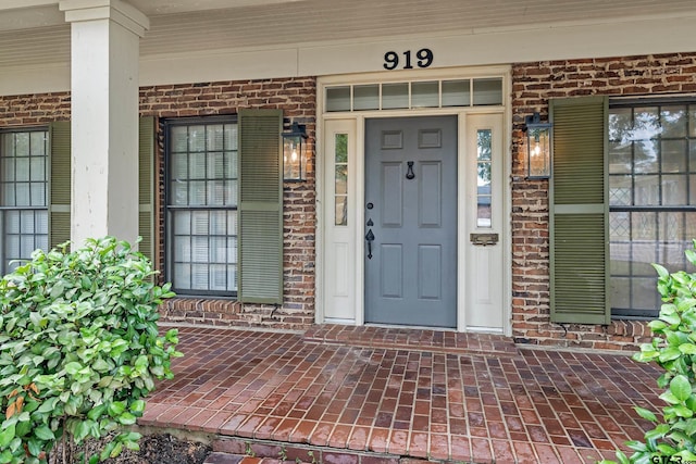 property entrance featuring a porch and brick siding