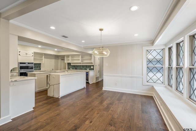 kitchen with visible vents, ornamental molding, a kitchen island, a chandelier, and dark wood-style flooring