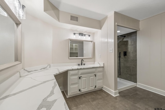 bathroom with vanity, baseboards, visible vents, and a tile shower