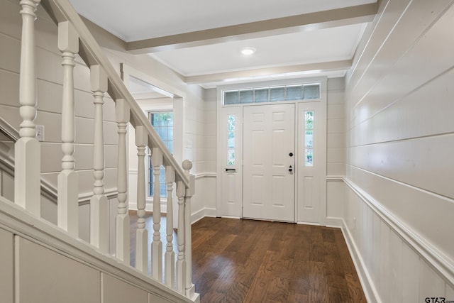 entrance foyer with beam ceiling, stairway, crown molding, a decorative wall, and dark wood-style flooring