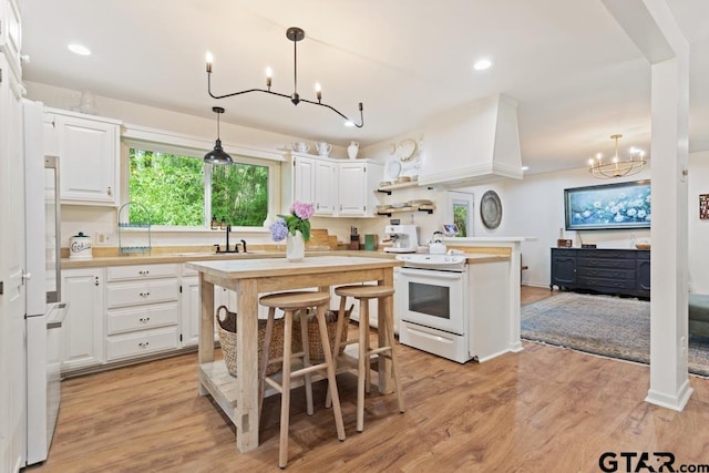 kitchen with hanging light fixtures, light hardwood / wood-style floors, white cabinets, white appliances, and a center island