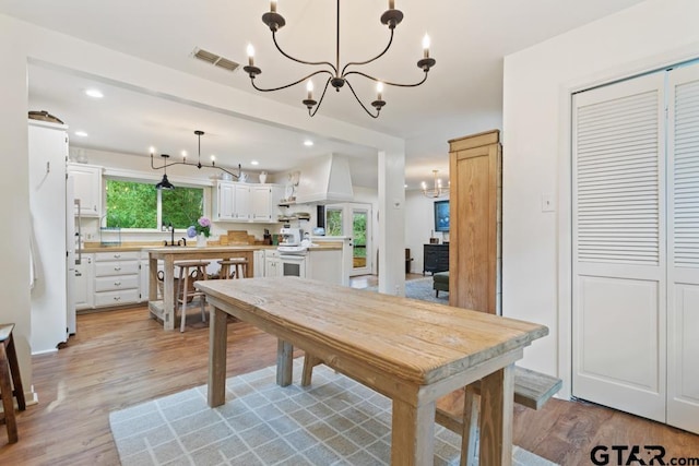 dining room with light wood-type flooring, sink, and a notable chandelier