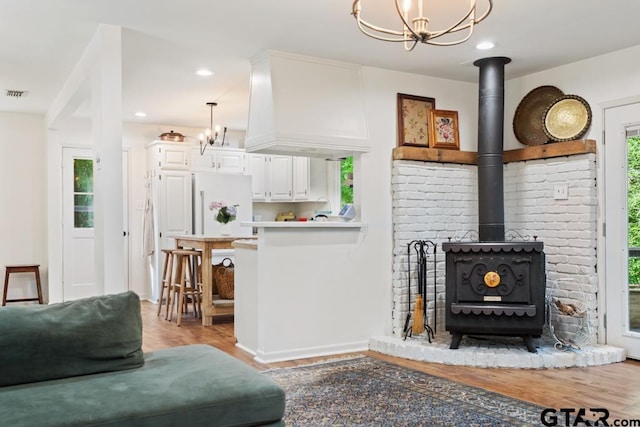 living room featuring light hardwood / wood-style floors, an inviting chandelier, and a wood stove