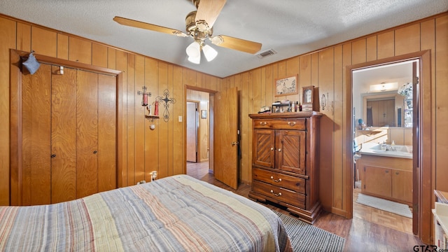 bedroom with a textured ceiling, ceiling fan, wooden walls, connected bathroom, and a closet