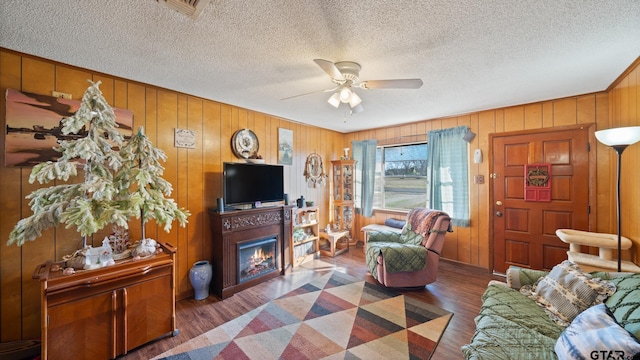 living room featuring ceiling fan, wooden walls, dark wood-type flooring, and a textured ceiling