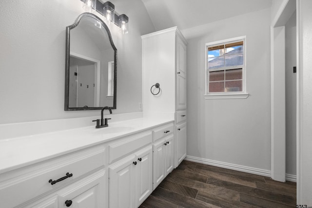 bathroom with lofted ceiling, baseboards, wood finished floors, and vanity