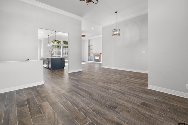 unfurnished living room featuring dark wood-style floors, a sink, crown molding, baseboards, and a chandelier